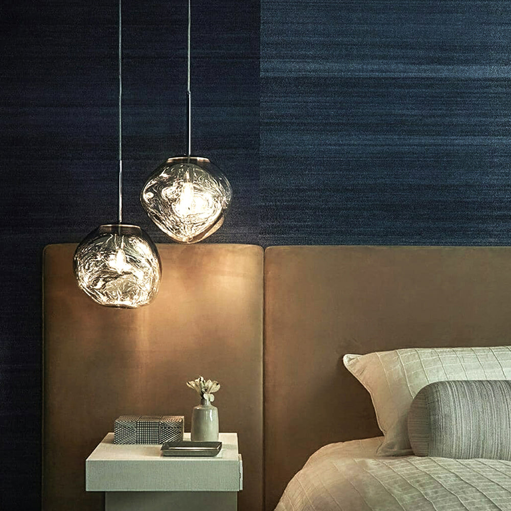 Two small Silver irregular pendants above a white bedside table beside a brown headboard and dark blue wall