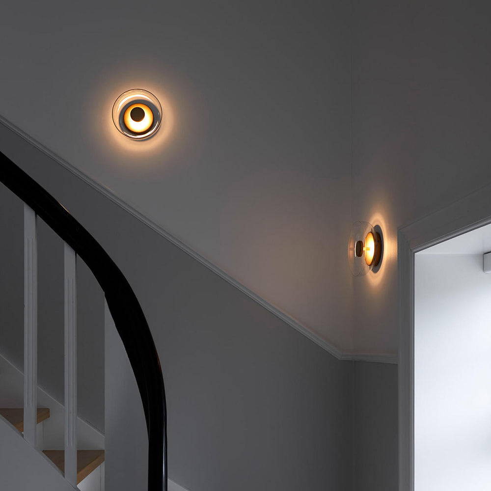 Two lit glass bowl wall lights by a curving black stair railing