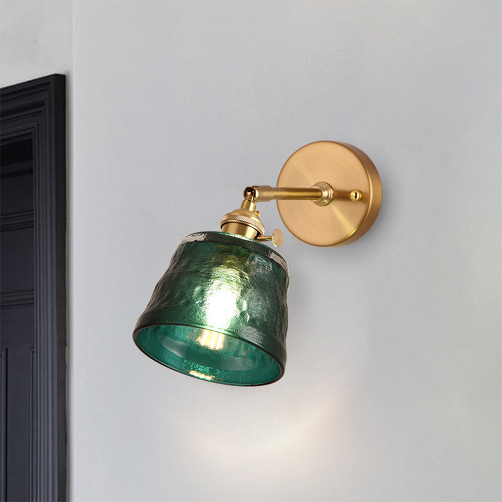Angled lit green textured shade with visible open rim on gold-tone arm near dark picture frame
