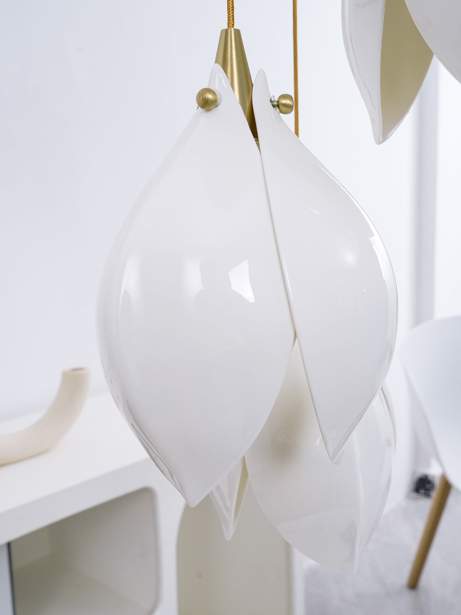 Unlit glossy white petal bud with gold-tone top before a pale arched console