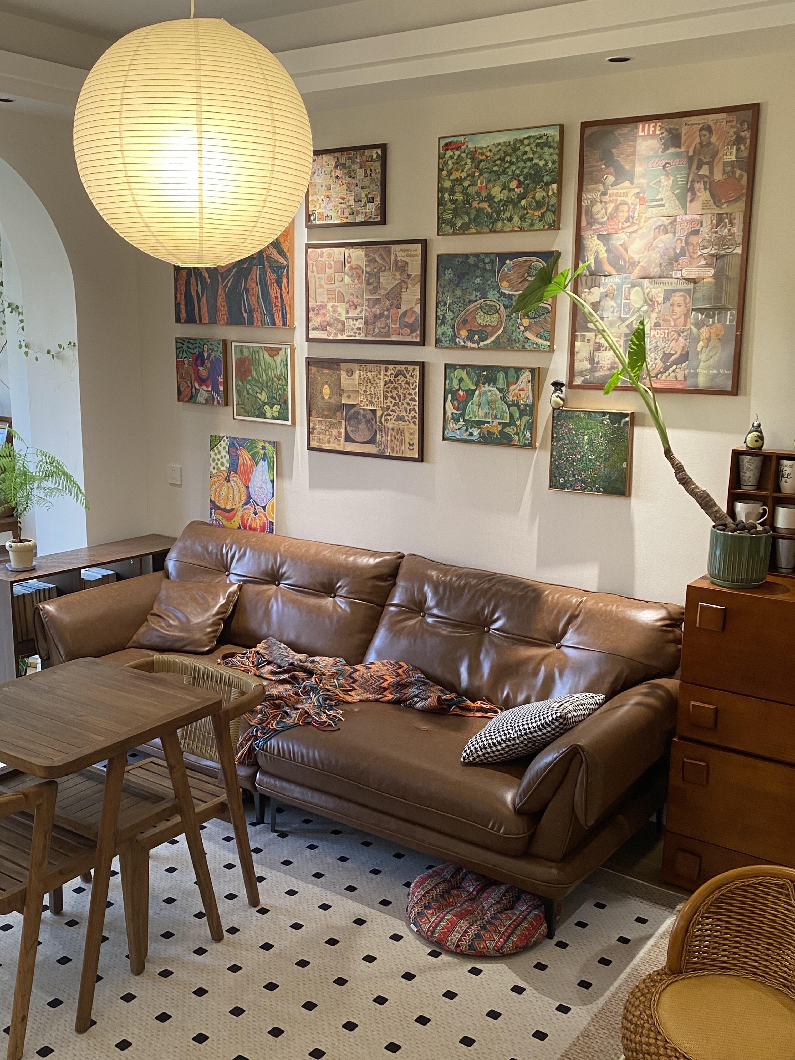Warm-looking globe above a brown leather sofa and wood coffee table beside collage artwork and a plant