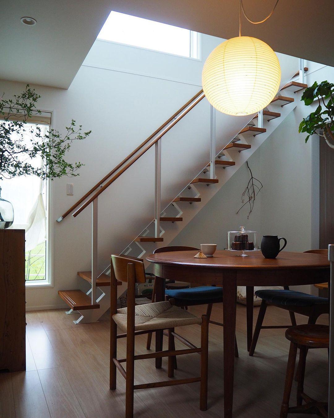 Close glowing globe above a wood dining table with cake and pitcher beside an open timber staircase