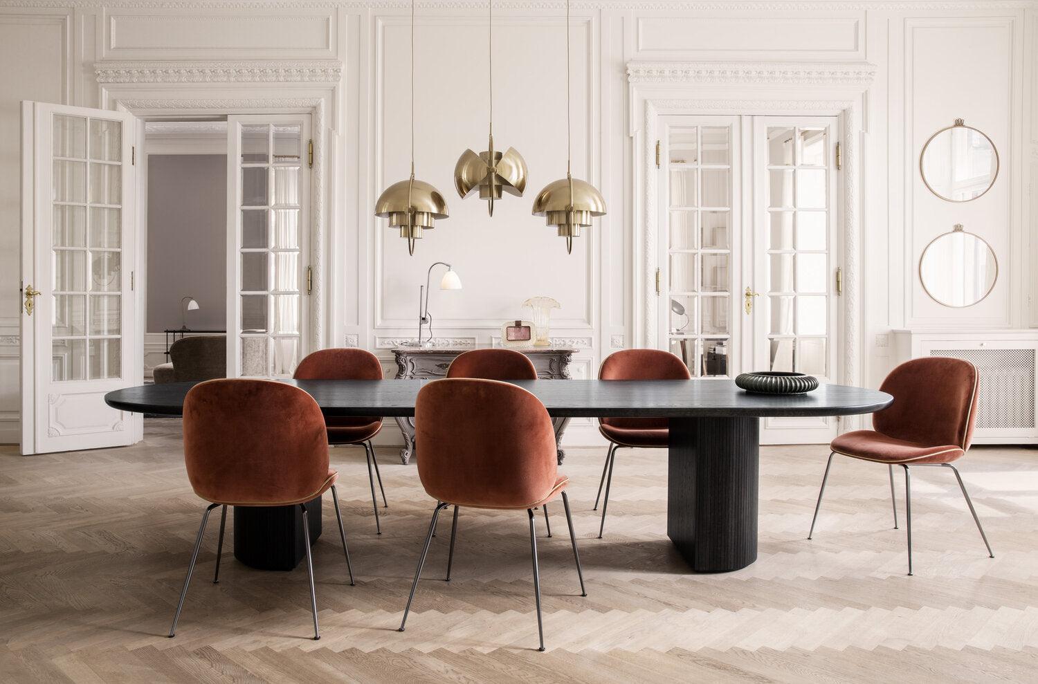 Gold-toned adjustable pendants above a dining table with rust-coloured seating.