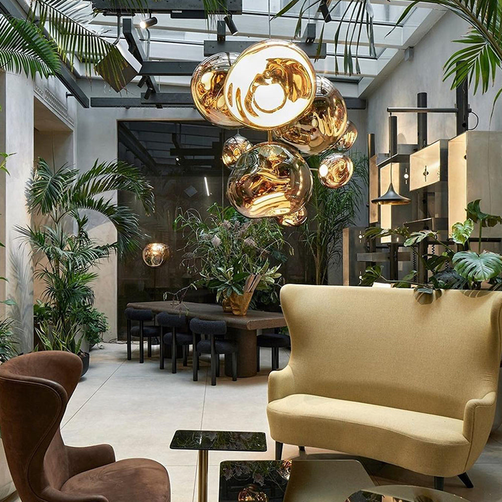 Gold irregular pendants in a glazed-roof lounge with plants, pale yellow and brown chairs and black glass tables