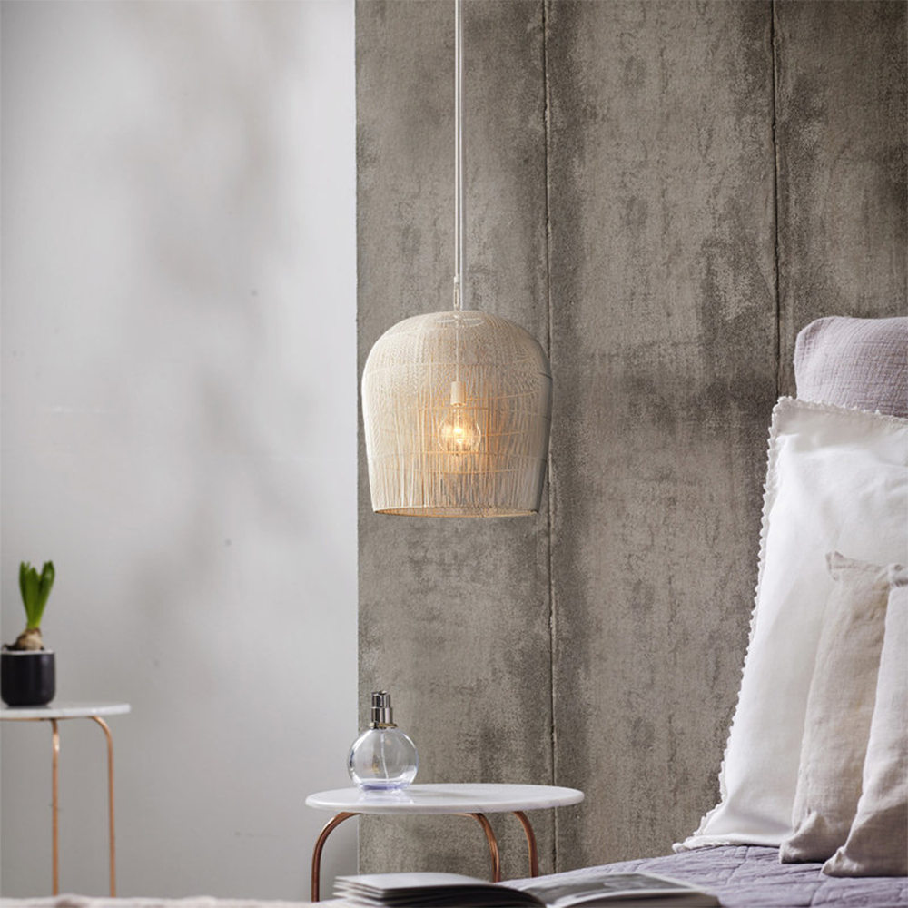 White rattan pendant beside pale bedding
