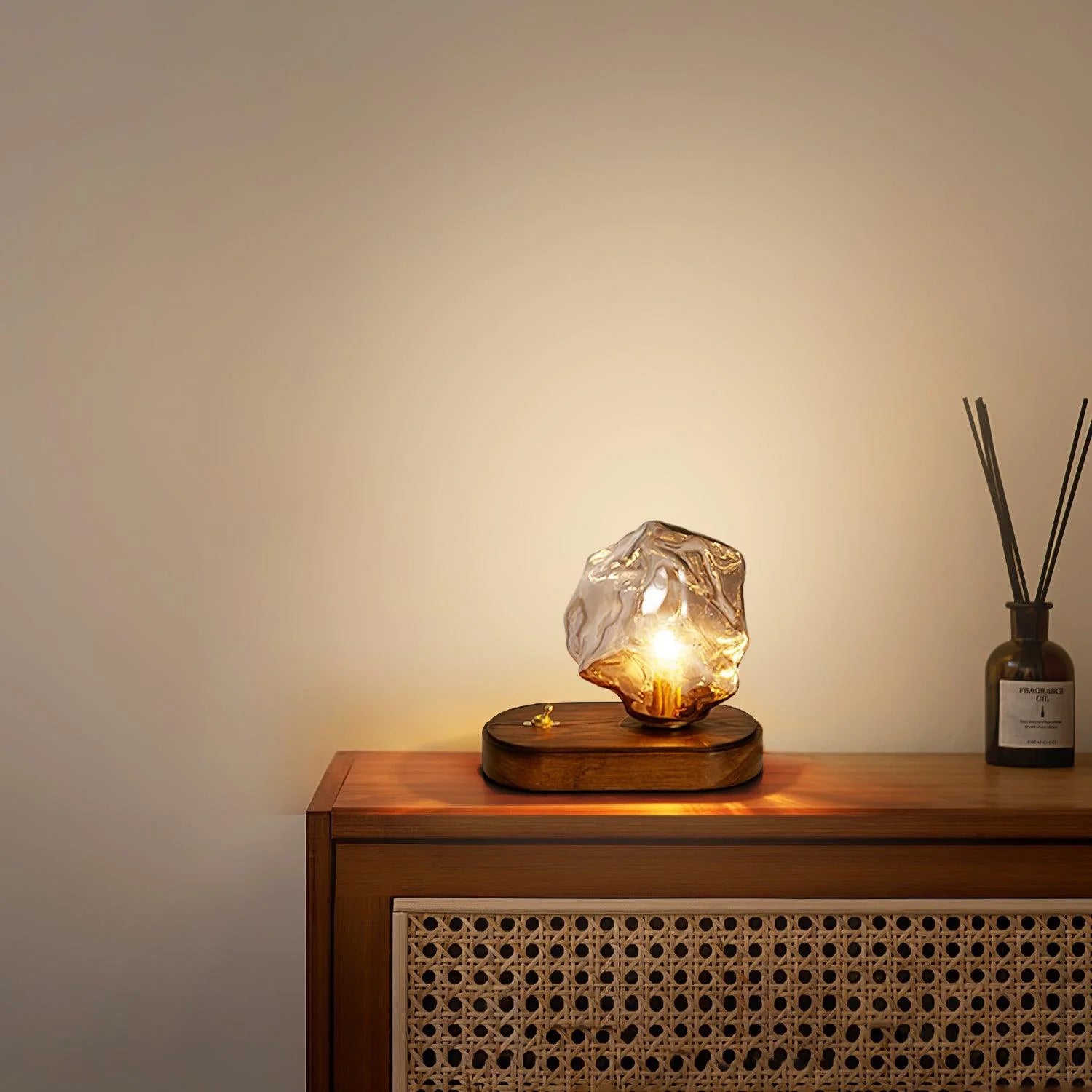 Ice Stone lamp on a wood cabinet with a woven cane front and a reed diffuser at right