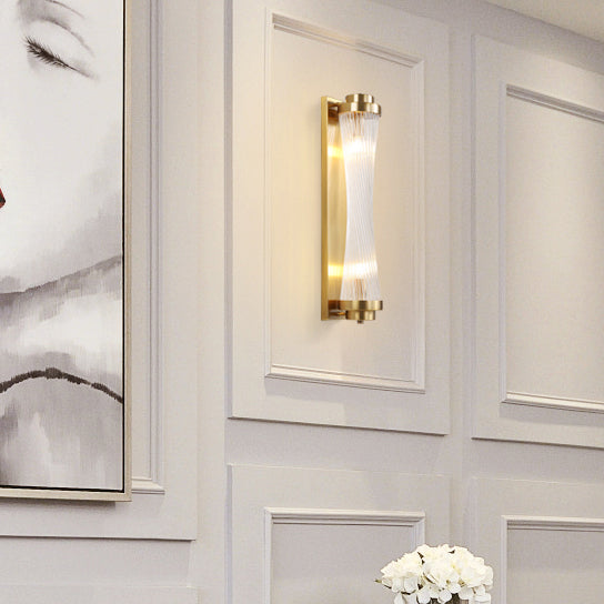 Gold Crystal Pillar wall light on a white decorative wall panel beside part of a portrait and flowers