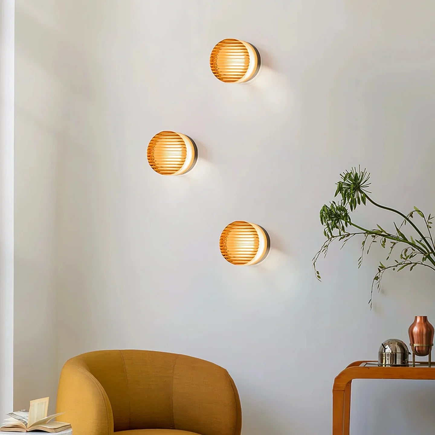 Three orange round wall lights above an ochre armchair, open book and wood console with metal vessels
