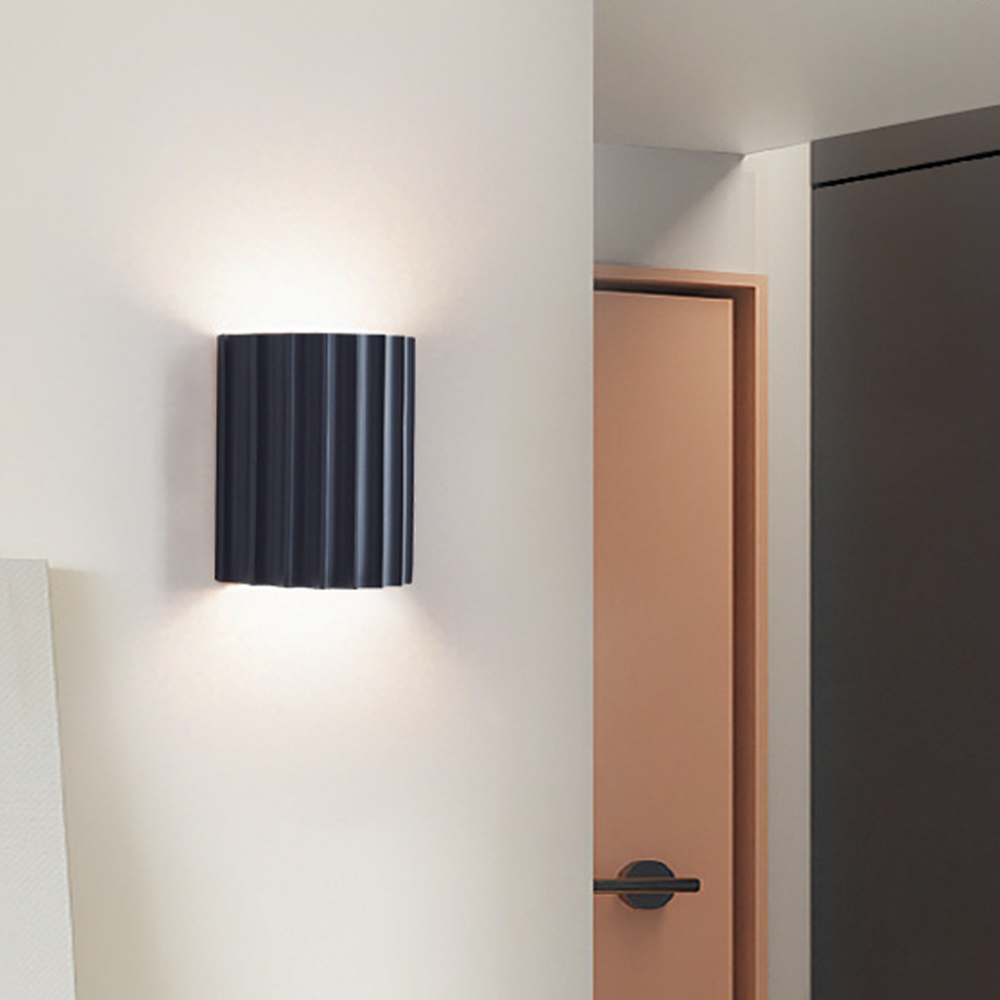 Dark grey fluted wall light on a pale wall beside a pink door and dark wall edge
