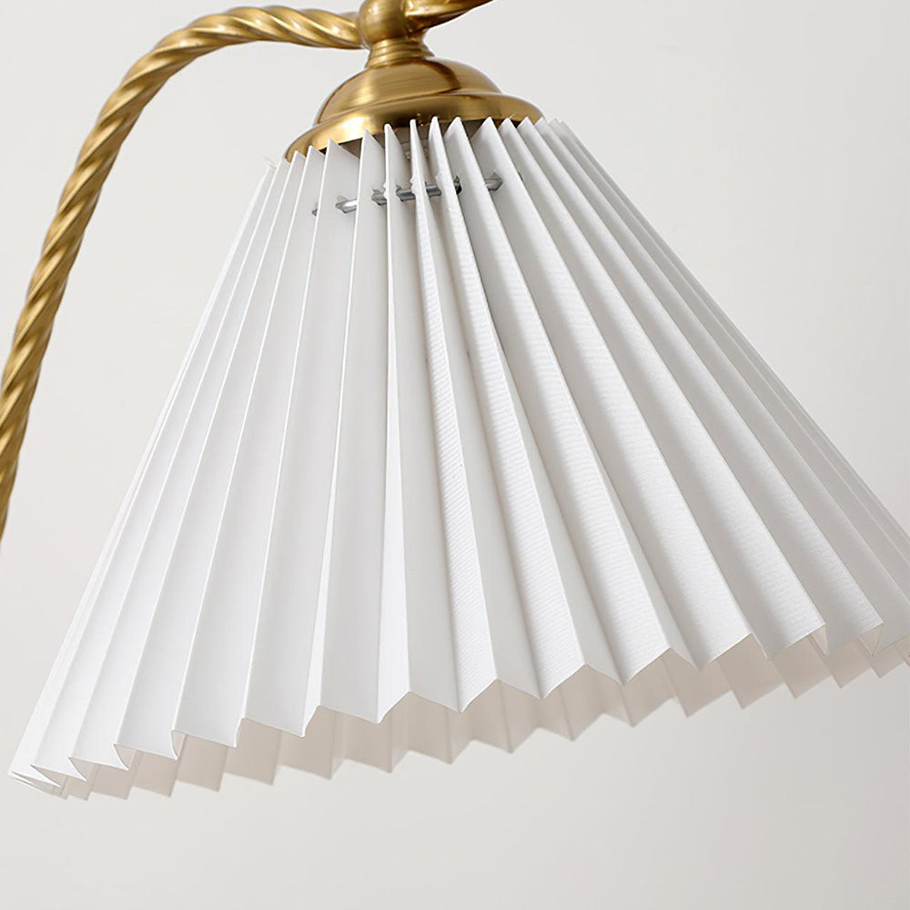 Close view of White fabric pleats beneath a gold-tone cap beside the twisted lamp stem