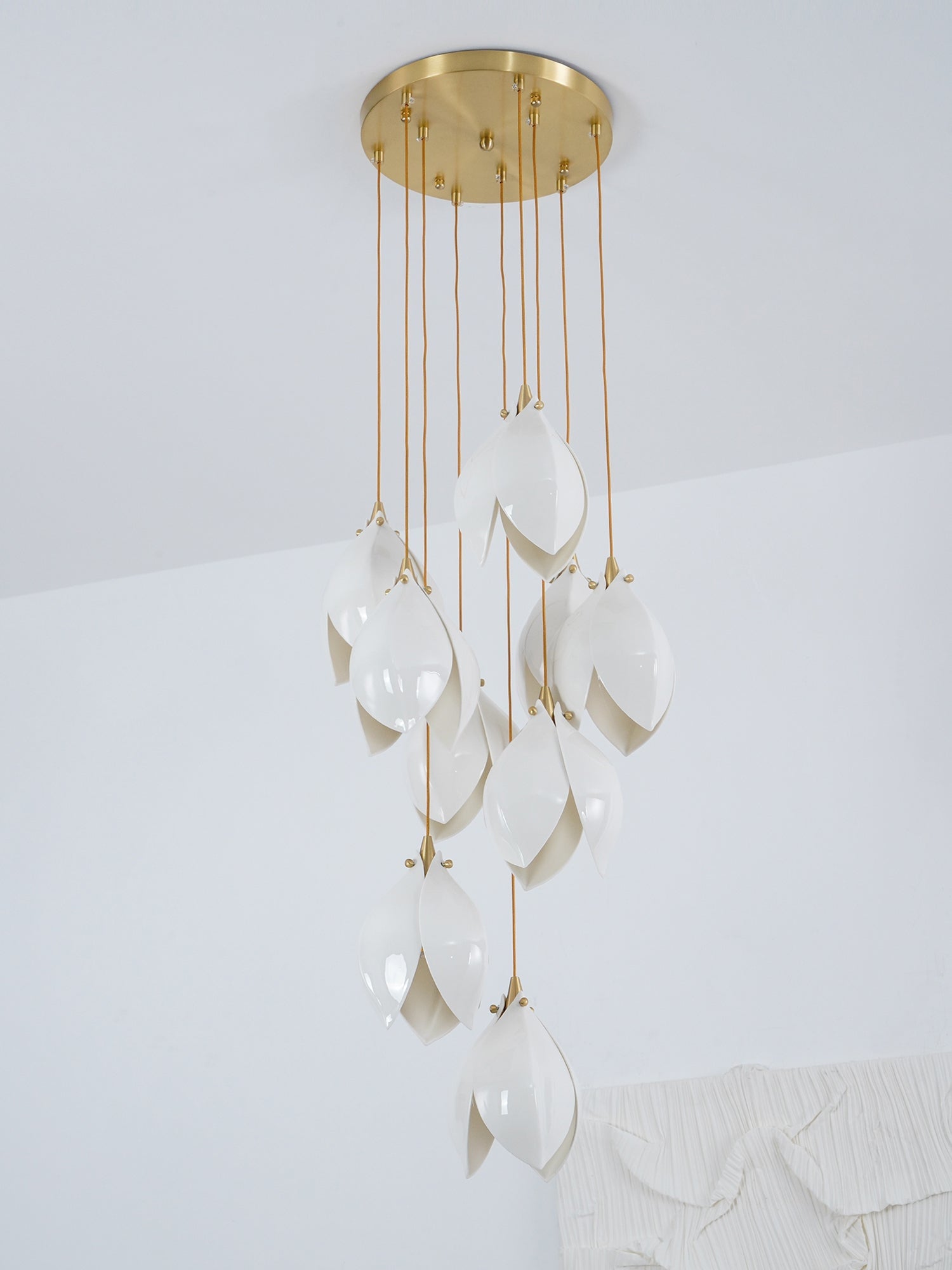 Ten white flower buds hanging from a round gold-tone canopy before pale wall art