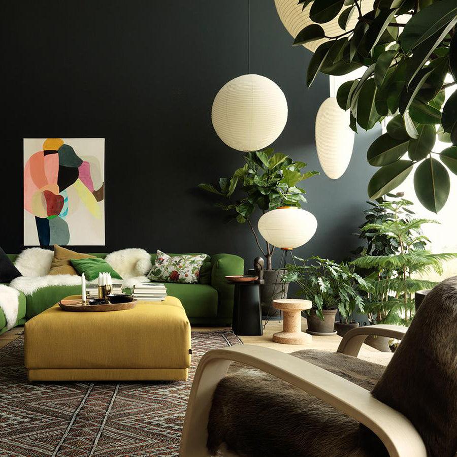 Paper globe and elongated paper lamps in a green room with green sofas, plants and a gold ottoman