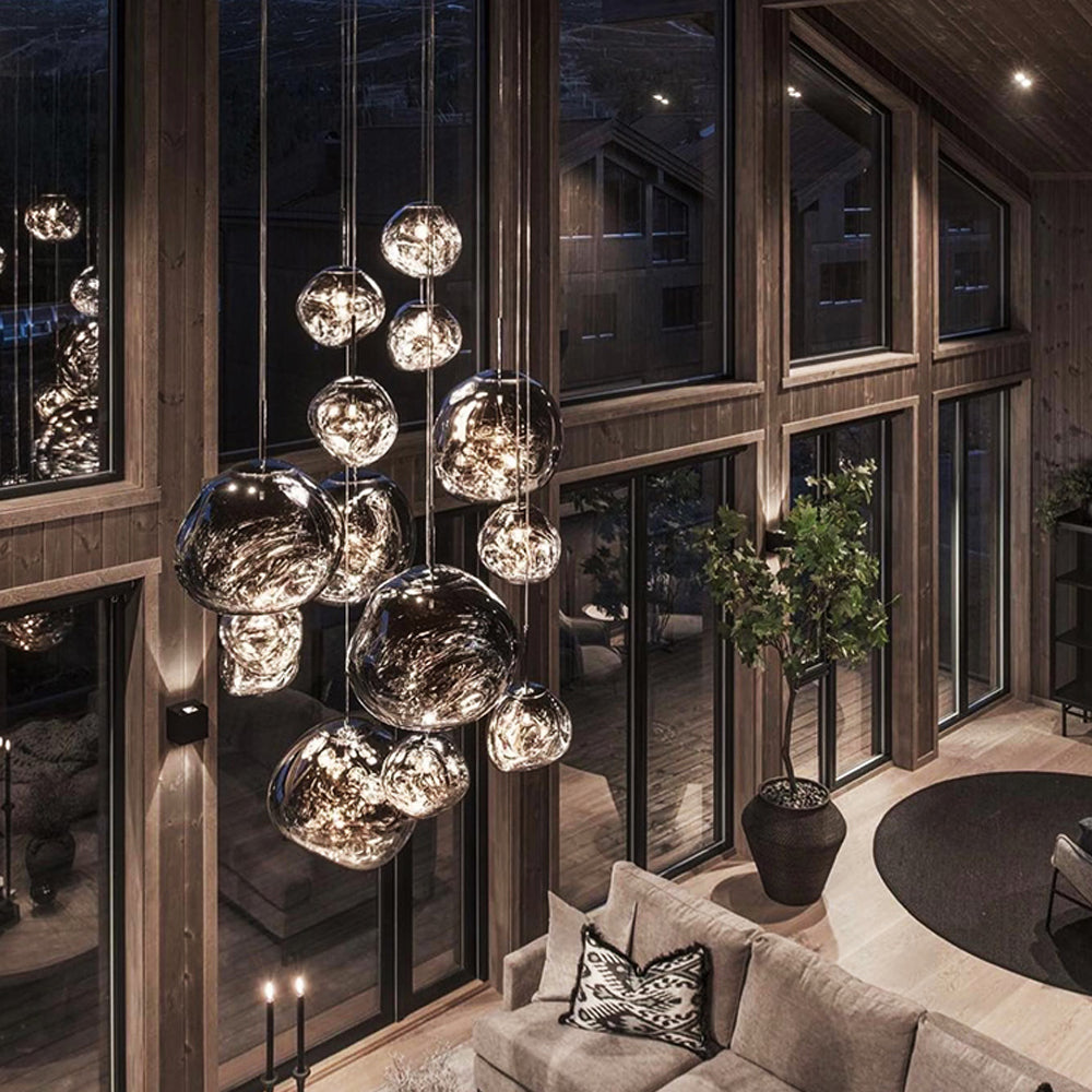 Smoky reflective pendants beside tall wood-framed windows above a pale sectional sofa, plant and round rug
