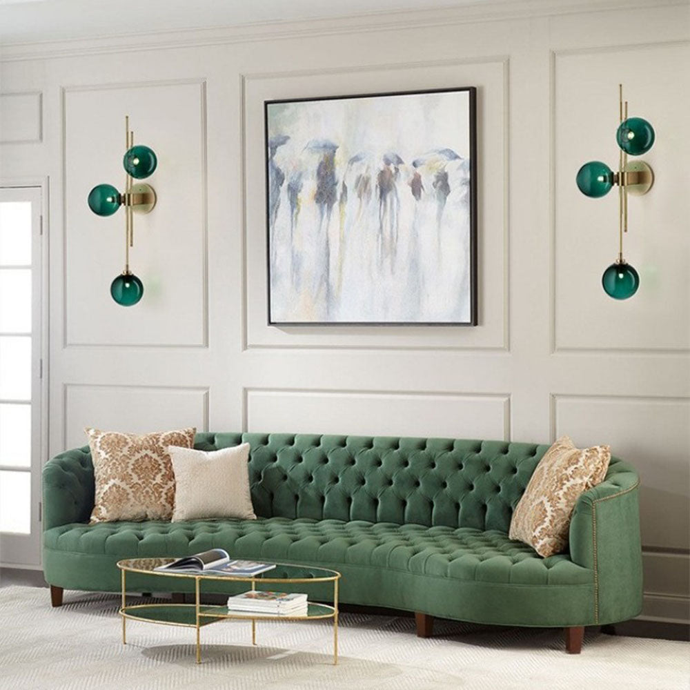 Two green three-globe wall lights flanking artwork in white wall panels above a green tufted sofa