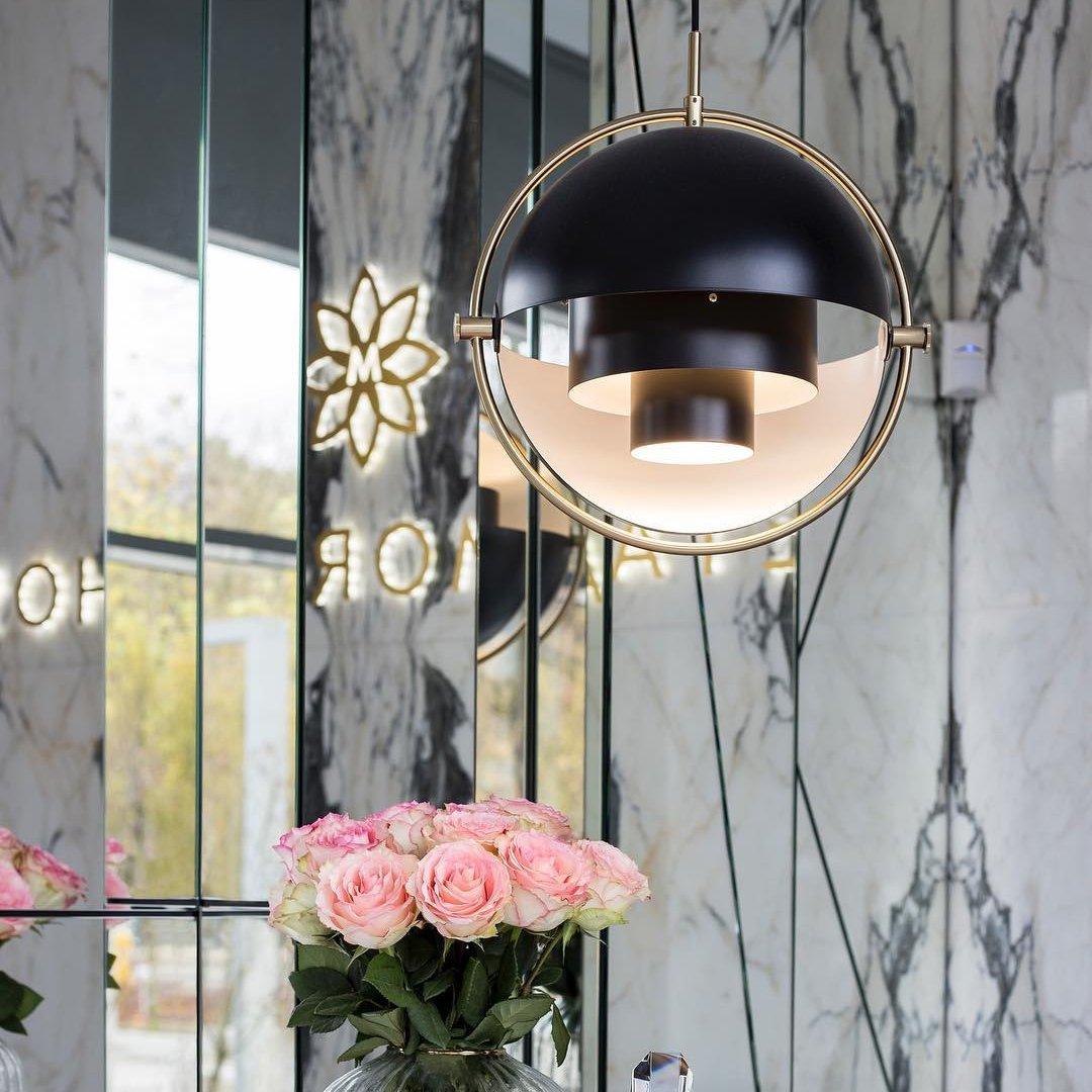 Black-and-gold ring pendant above pink roses beside a veined stone wall.