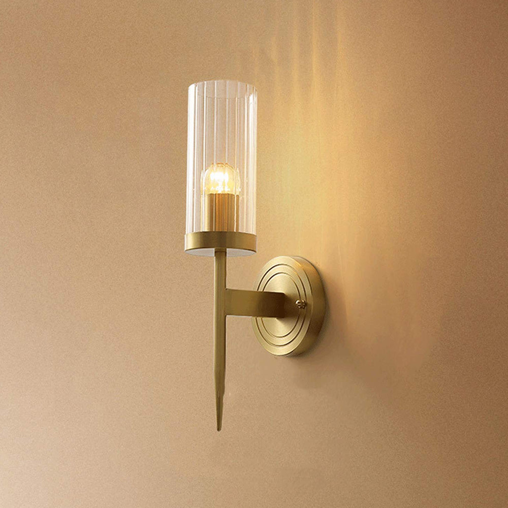Lit single-arm ribbed wall light with gold-tone concentric plate and tapered stem on a pale wall
