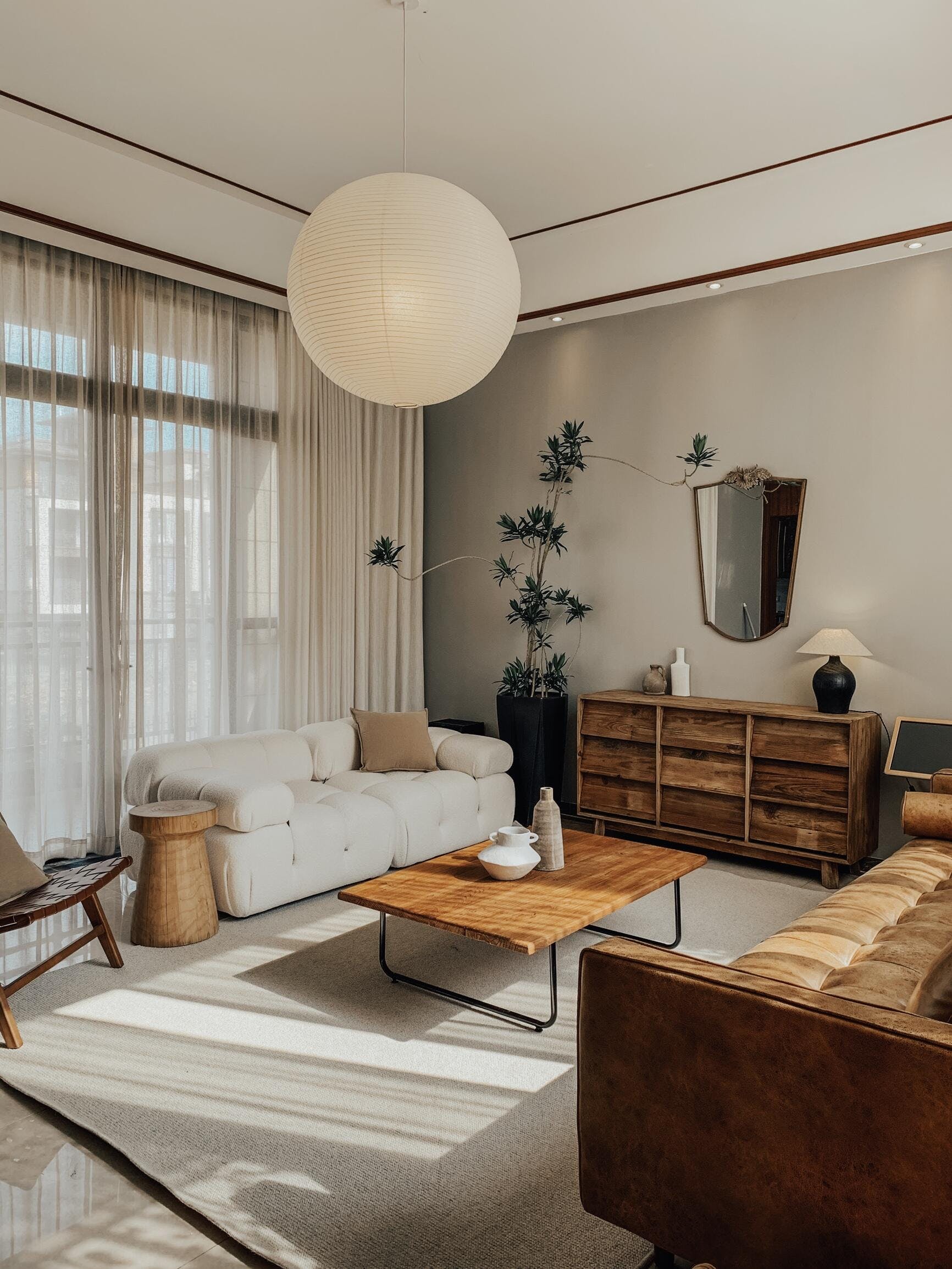 Large White globe above a coffee table near white and brown sofas, dresser, mirror and tall plant