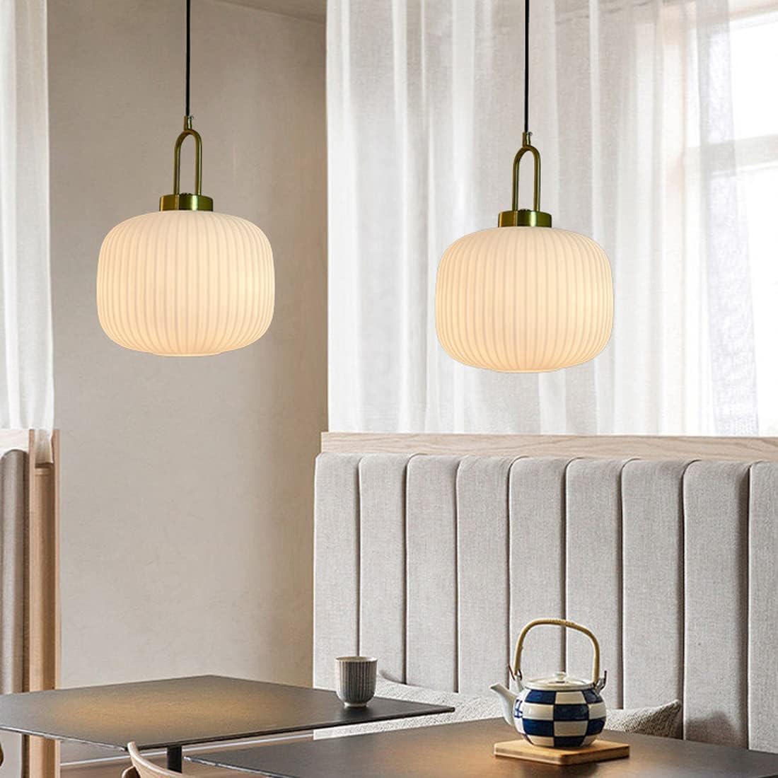 Two white ribbed glass pendants above tables and a banquette beside sheer curtains