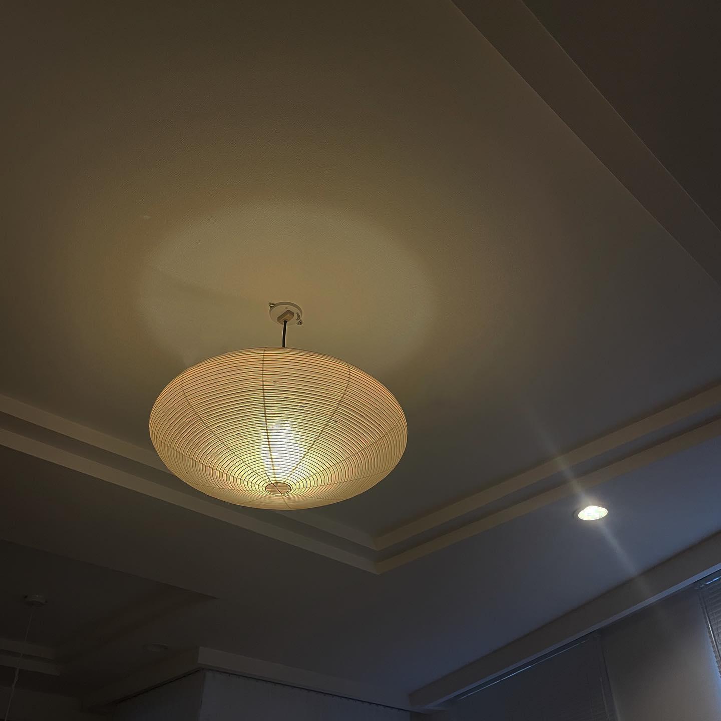 Underside of a glowing ribbed paper shade on a short dark cord below a white ceiling plate