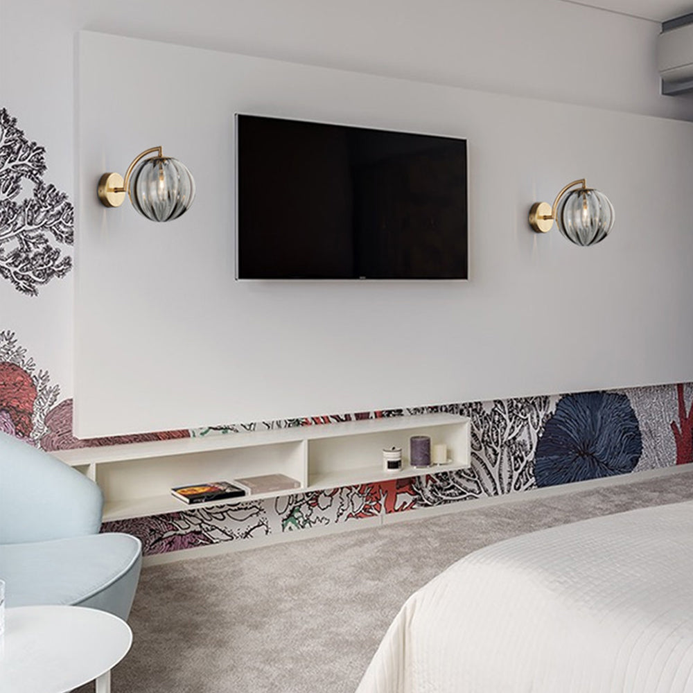 Two smoke-grey globe lamps beside a television, with open shelving, patterned wallpaper, pale chair and bed