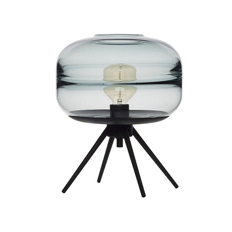 Unlit blue-tinted glass shade with a visible bulb and its reflection above four black splayed legs against white