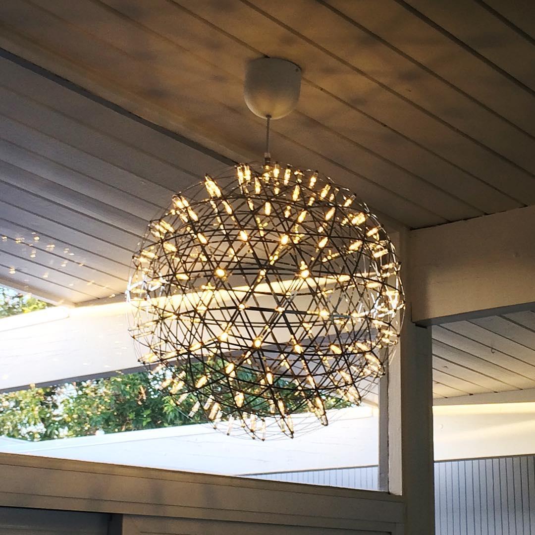 Glowing sphere pendants beneath a covered slatted roof near an outdoor setting