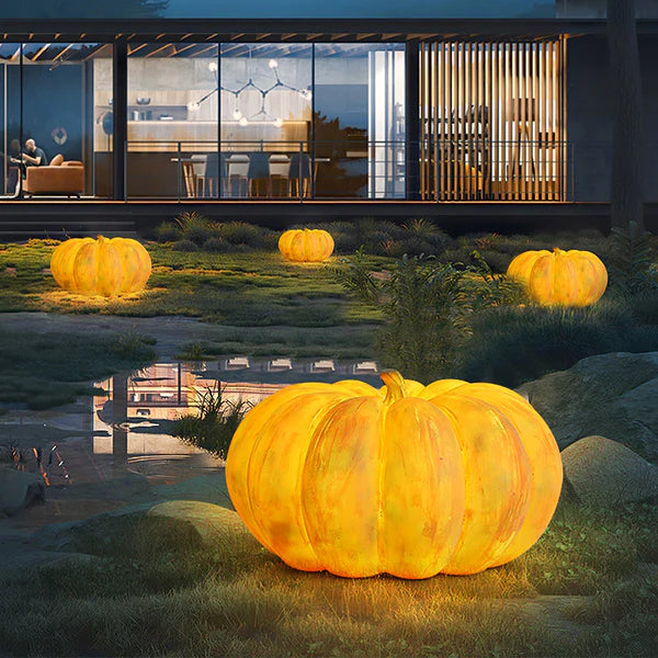 Four glowing pumpkin lamps among grass, rocks and reflective water before a glass-front house at dusk