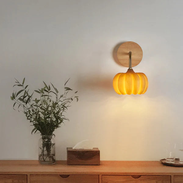 Yellow pumpkin wall light above a wooden cabinet with a foliage vase and tissue box