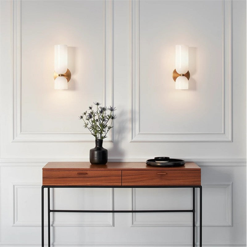 Two White glass wall sconces above a wooden console with black vase and stacked plates