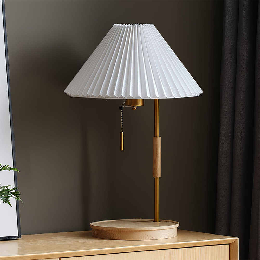 Unlit lamp with a pale wood base and stem sleeve, white pleated shade and hanging chain on a wood cabinet