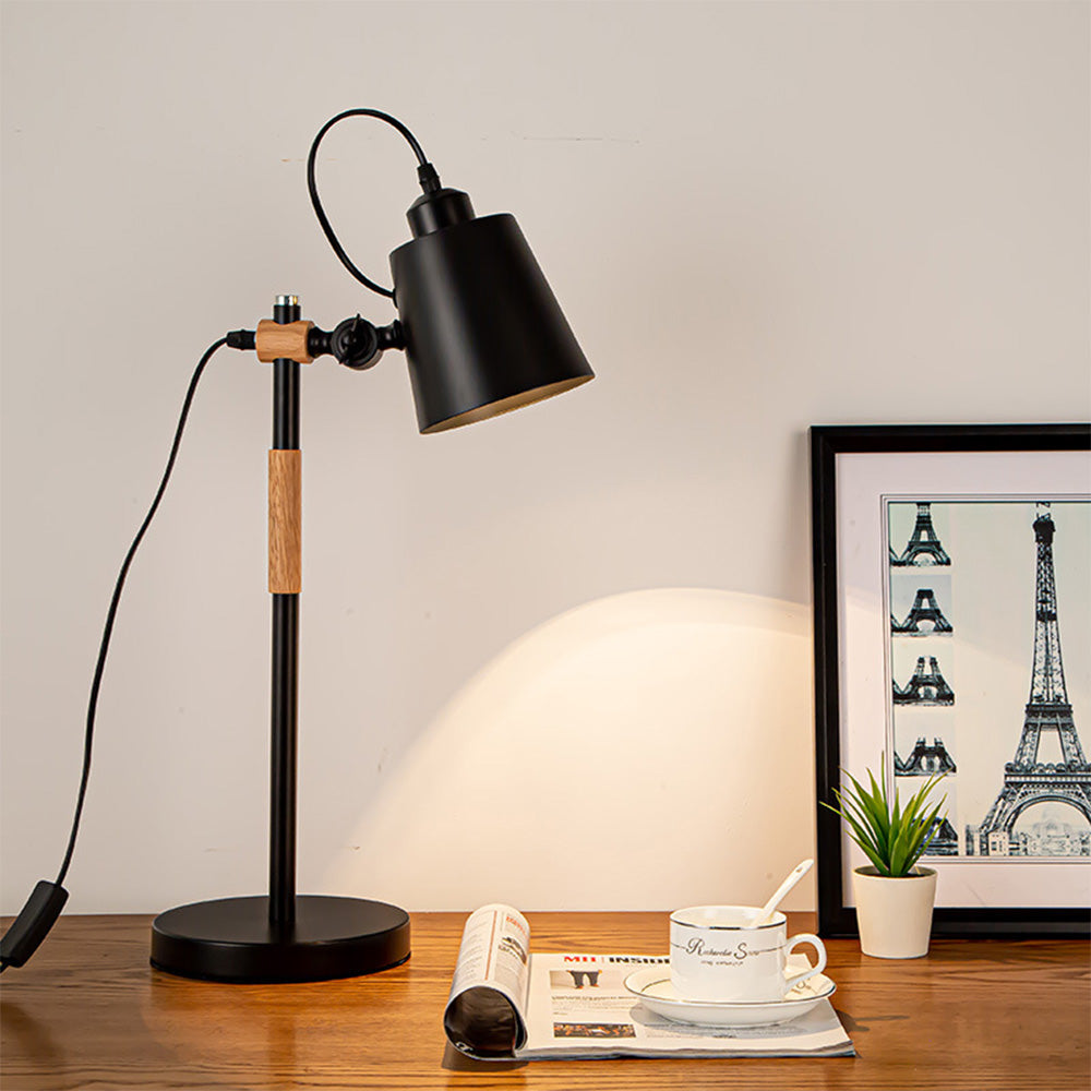 Black tapered-shade lamp with wood details on desk beside magazine, cup, small plant and Eiffel Tower print, with cord module at left