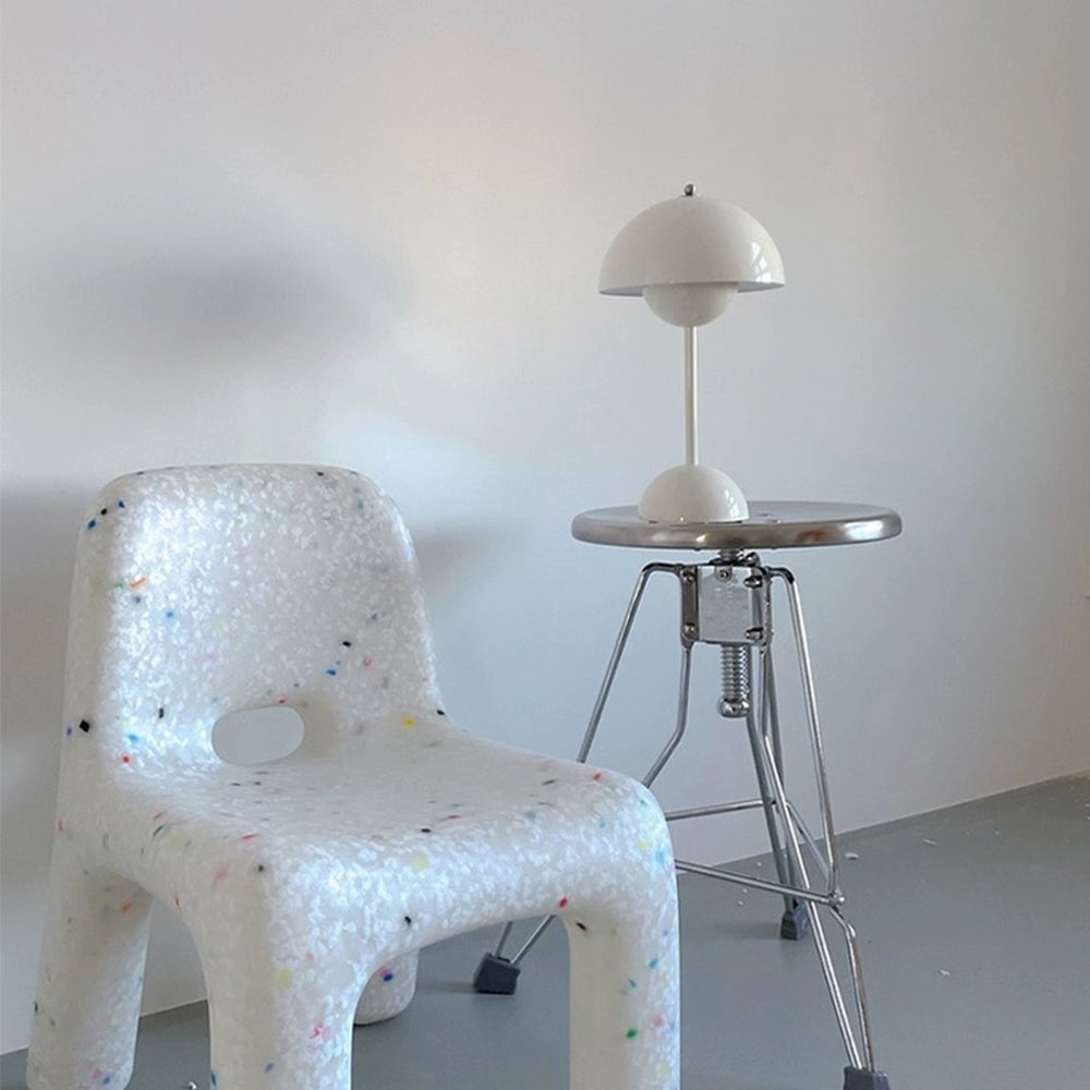 White dome table lamp on a reflective metal stool beside a speckled chair