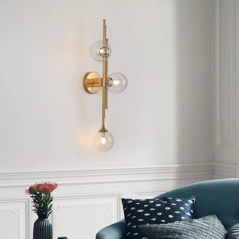 Lit clear-globe wall light above a curved blue-green sofa with patterned cushions beside a flower vase