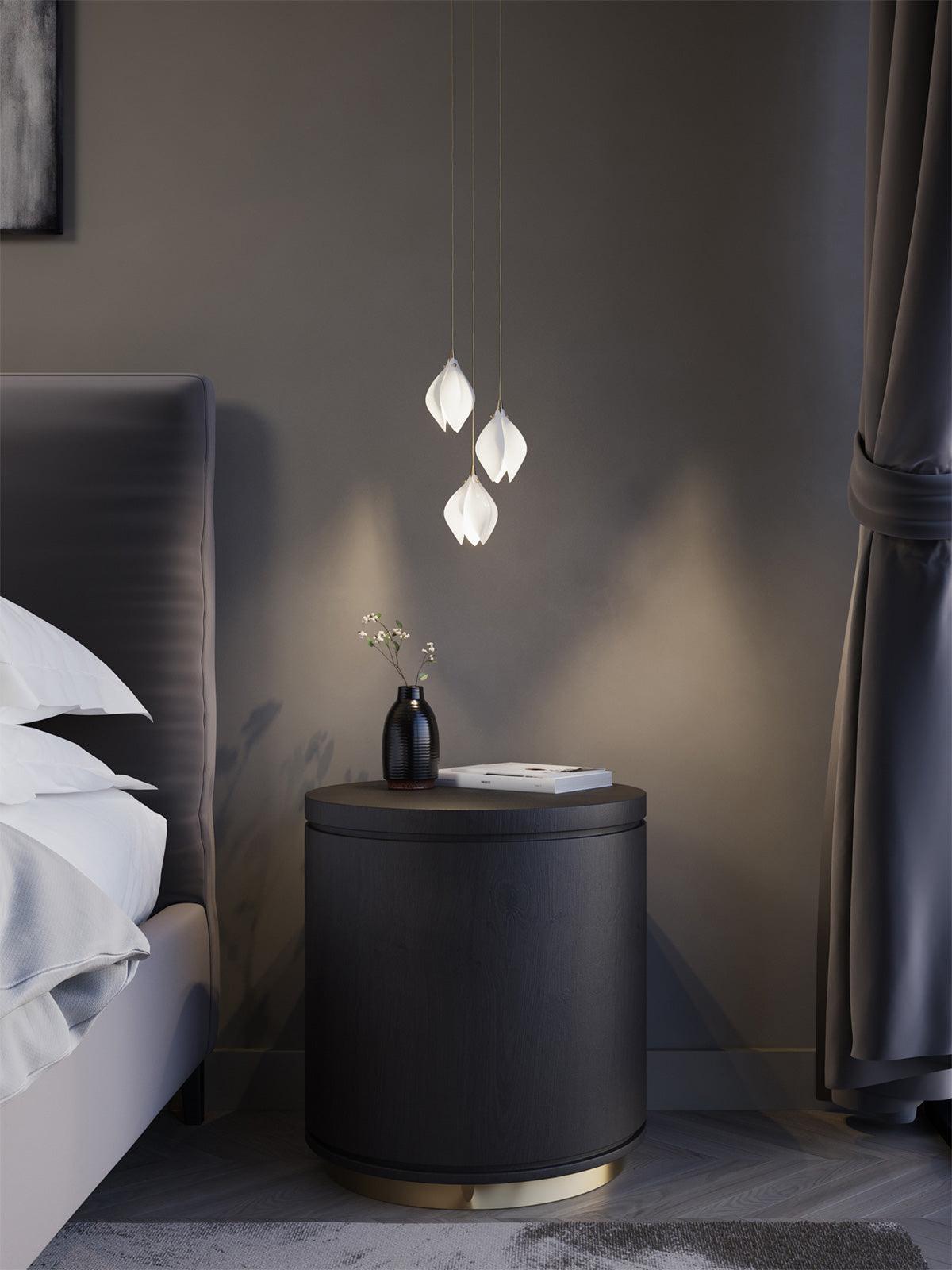 Three glowing flower buds above a dark bedside cabinet beside a padded bed