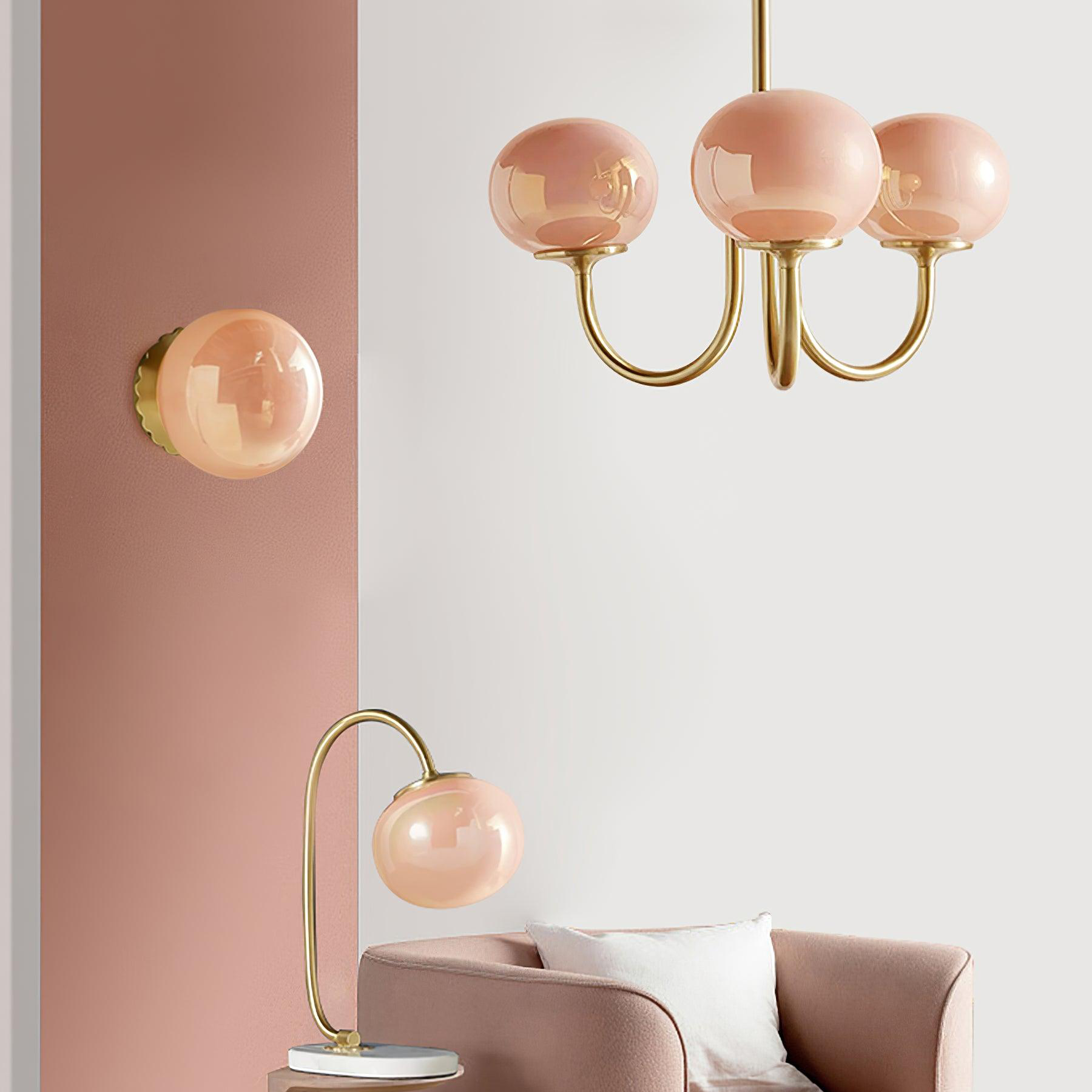 Pink three-globe chandelier over an armchair, beside a separate wall light and curved table lamp
