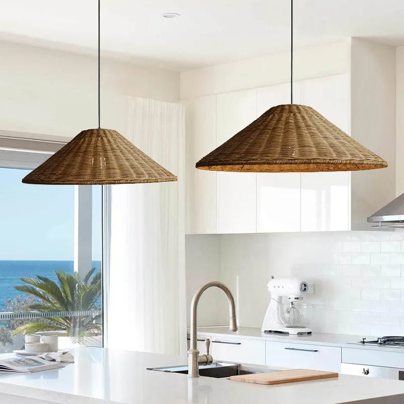 Two Brown woven pendants above a white kitchen island beside a window overlooking palms and the sea