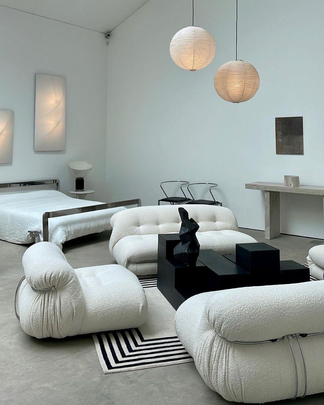 Two glowing globes at staggered heights above white curved sofas and a black geometric coffee table