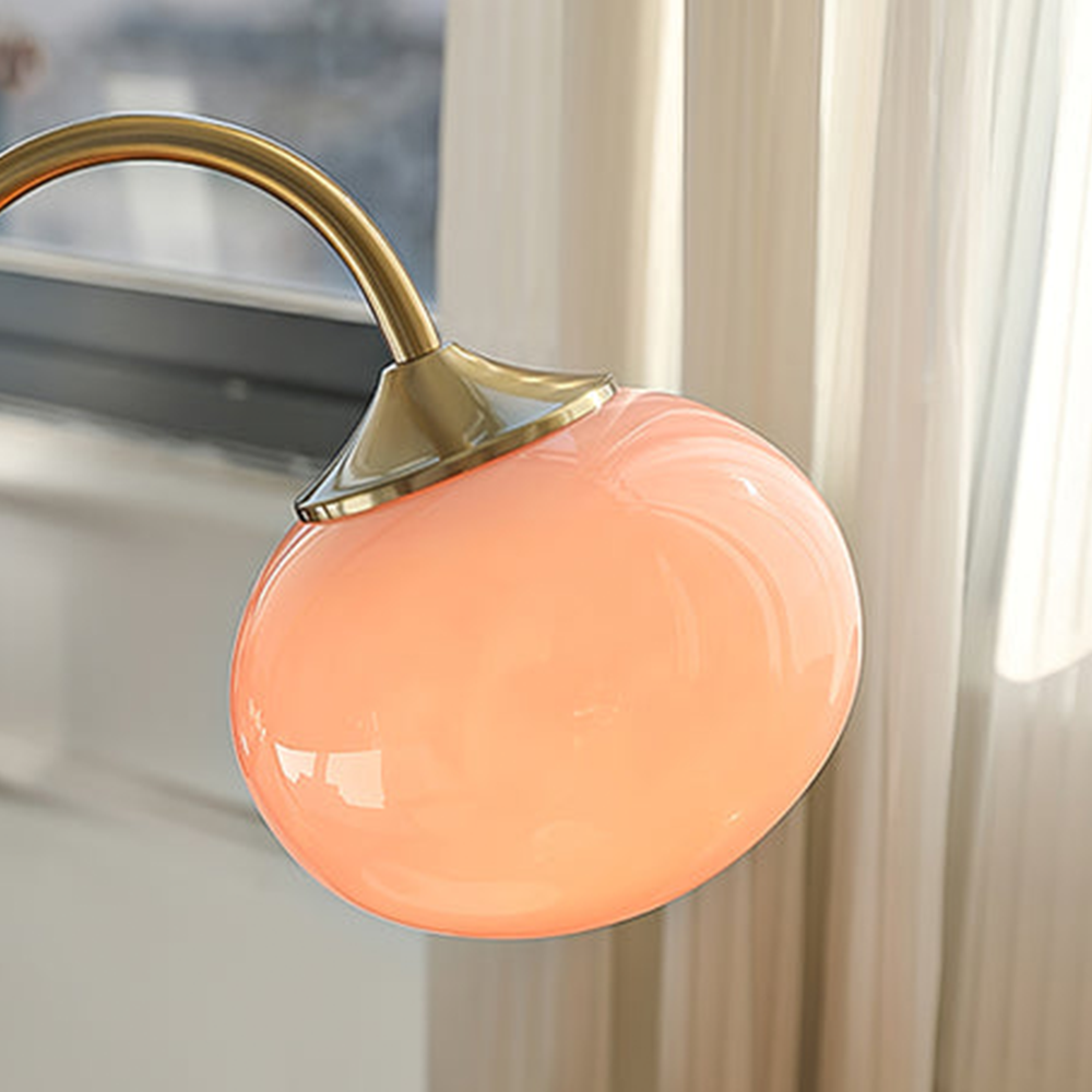 Close view of the illuminated pink globe shade and gold-tone cap against cream curtains