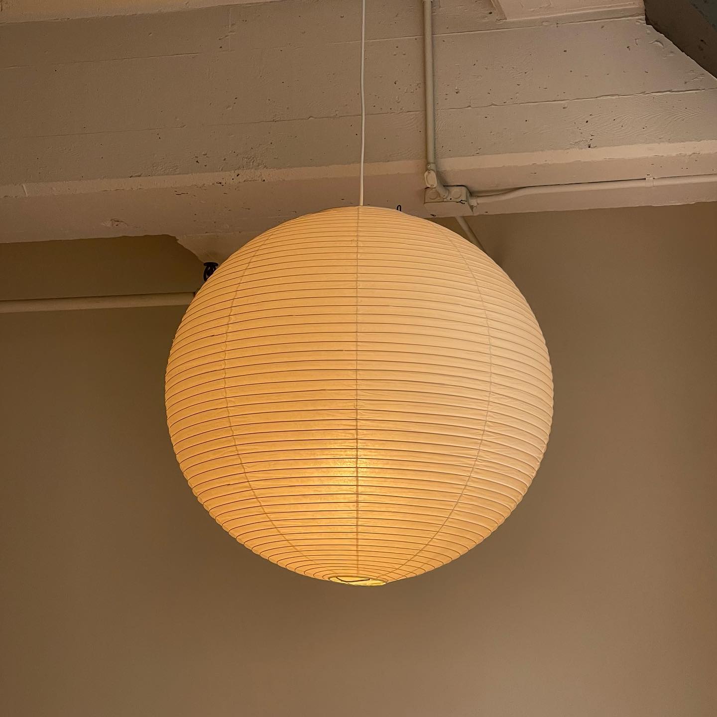 Glowing ribbed paper globe below a concrete ceiling beam and exposed conduit