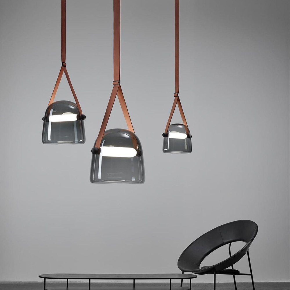 Three brown-strapped smoked glass pendants above a low table beside a black chair