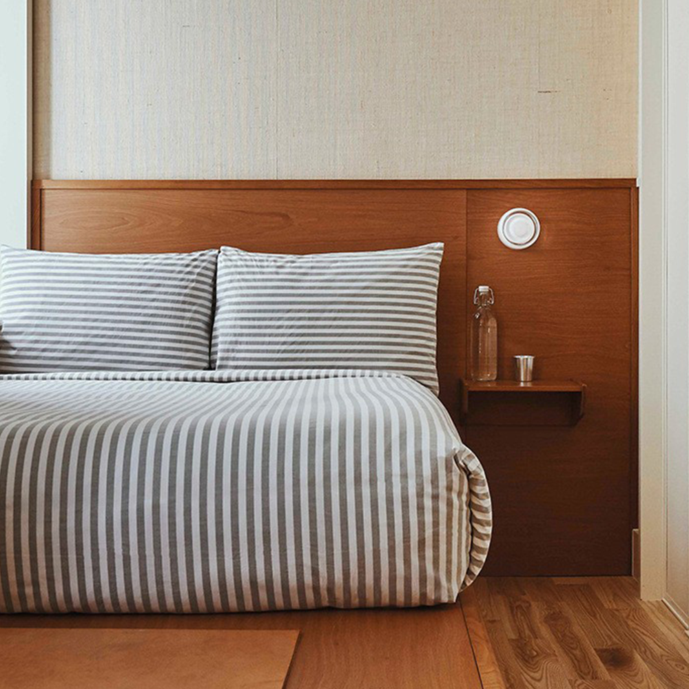 White round wall light on a wooden headboard above a bedside shelf beside a striped bed