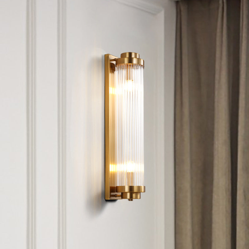 Lit Gold straight-rod wall light on white wall mouldings beside a brown curtain