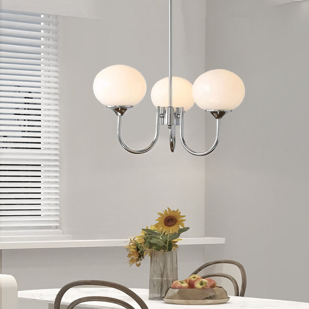 Three illuminated white globes on chrome-tone arms above a dining table with sunflowers and fruit