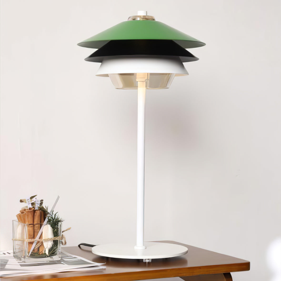 Layered green Overlay lamp on a wooden table beside papers and a glass vessel; cord behind the white round base