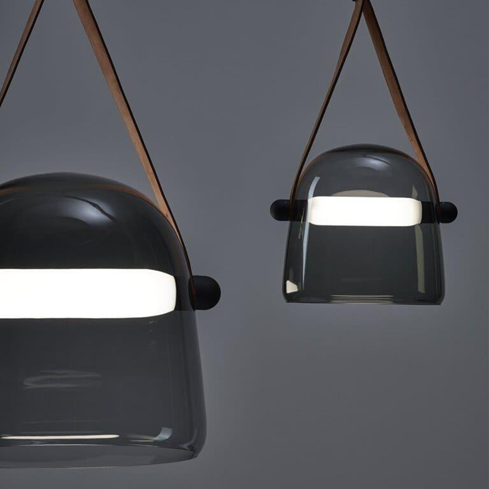 Close-up of two smoked glass pendants with brown straps, round side attachments and white light bars
