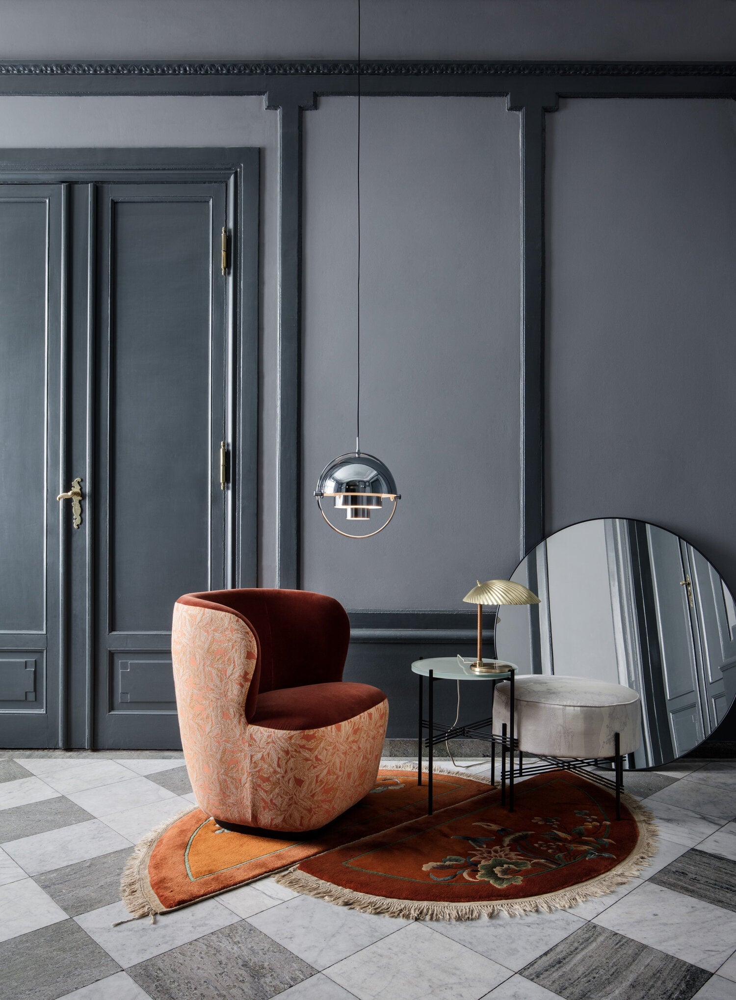 Chrome circular-frame pendant above a rust-coloured chair in a dark blue room.