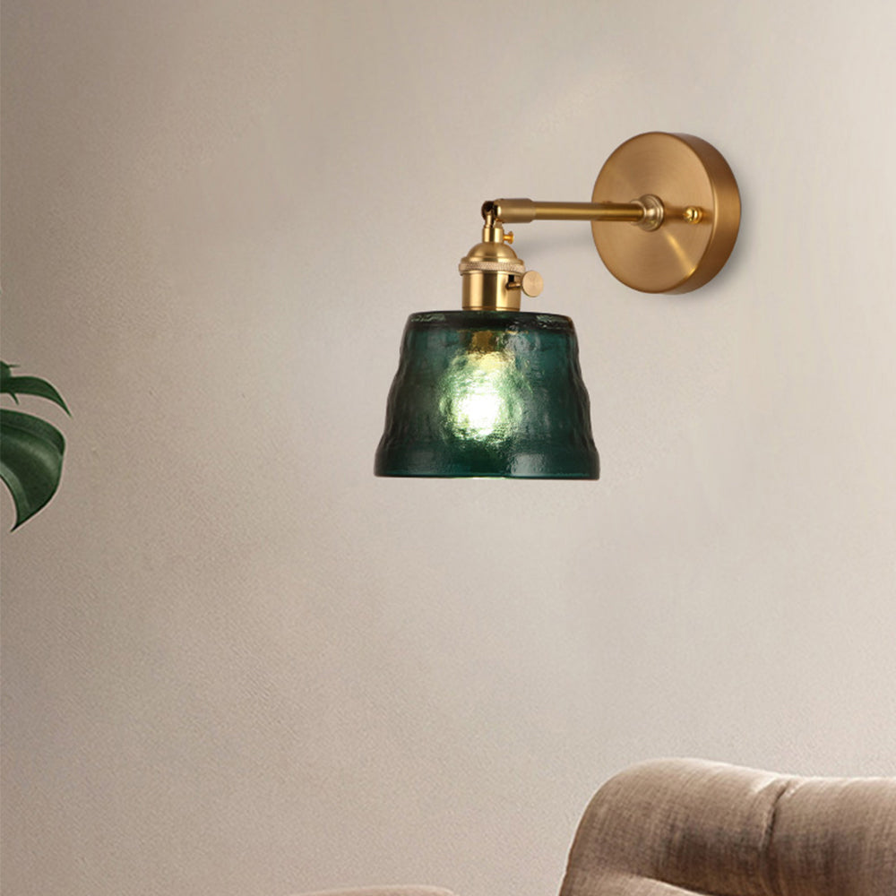 Side view of green textured wall light above beige tufted sofa with cropped green foliage at left