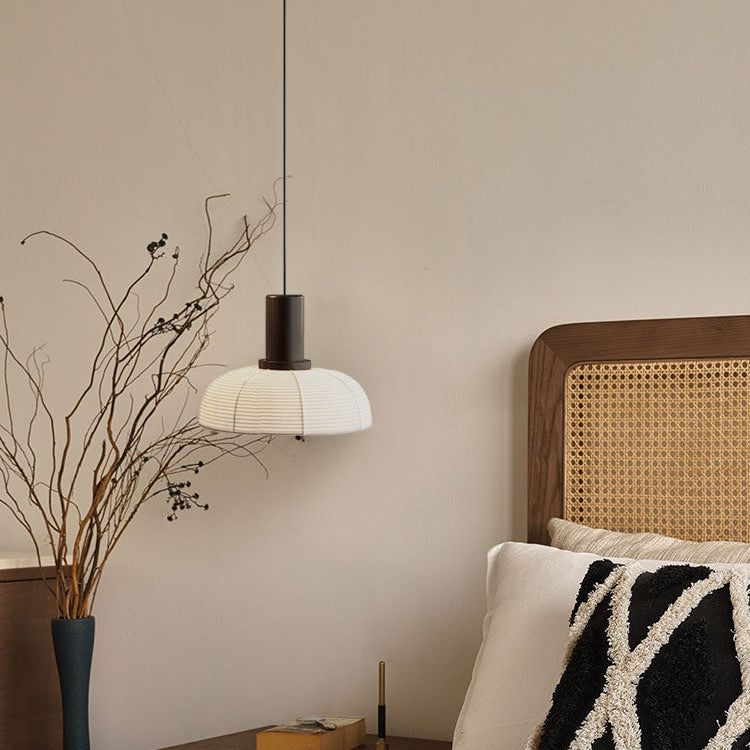 Single-dome ribbed pendant with a tall dark cylinder beside a cane headboard and pillows