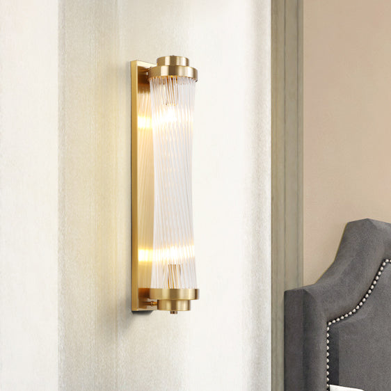 Gold wall light with a twisted-looking glass-rod pattern beside a grey upholstered headboard