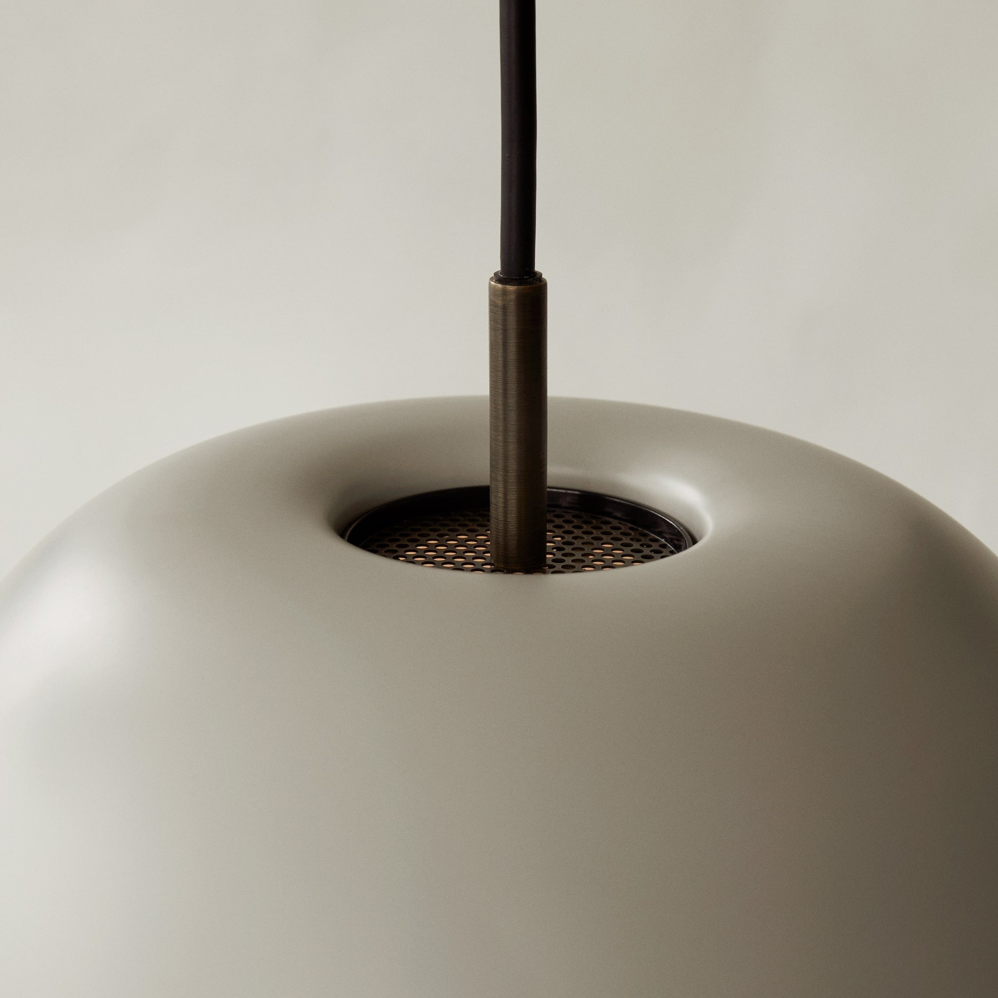 Close-up of a pale shade top, black cord, upper connector and circular perforated recess